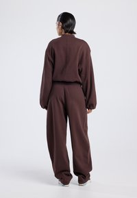 Brown fleece sweatshirt with oversized fit and dropped shoulders, paired with matching baggy sweatpants. Smooth texture and elastic waistband.