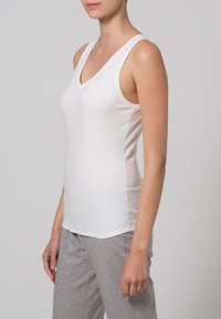 White sleeveless top with a V-neck design, made from soft fabric, featuring smooth texture and slim fit. Paired with gray pants.