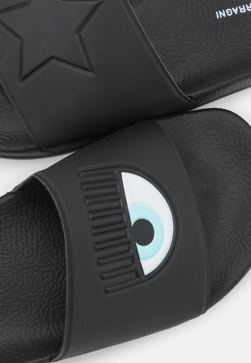 Schwarze Rutschsandalen aus strukturiertem Gummi. Ein Riemen verfügt über ein erhabenes Sternmuster; der andere hat ein Augenmotiv mit blauen Akzenten.