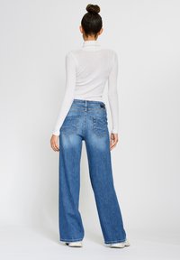 Wide-leg blue denim jeans with a high waist, featuring back pockets and subtle fading. Worn with a fitted white ribbed long-sleeve top.