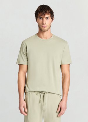 Maglietta a maniche corte di un verde chiaro e morbido, con collo tondo, texture liscia e design minimalista, abbinata a pantaloni coordinati.