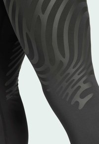 Mustat urheiluleggingsit, joissa on rakennegradientti erisävyisissä tummanharmaissa väreissä. Materiaali näyttää sileältä ja joustavalta.