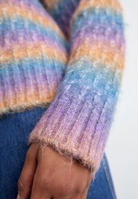 Pull en laine multicolore avec des rayures horizontales dans des teintes pastel de violet, bleu et orange. Poignets côtelés avec une texture douce.