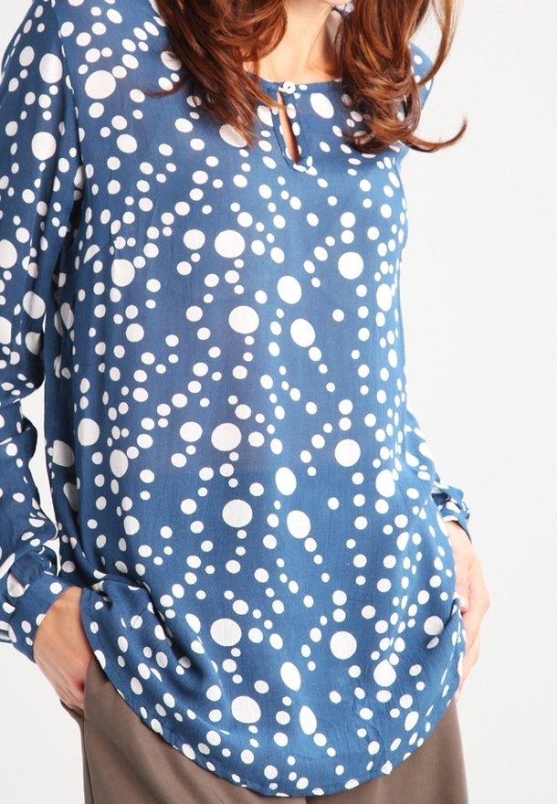 Blusa blu a maniche lunghe con pois bianchi, caratterizzata da un collo rotondo e un dettaglio a chiave sul davanti. Tessuto morbido e leggero.