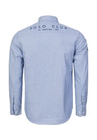 Vaaleansininen pitkähiha.paita, jossa on napillinen kaulus, kirjailtu "POLO CLUB"-logo ja hihansuut nappeineen. Sileä kangaspinta.