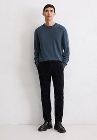 Męski ciemnoniebieski sweter z okrągłym dekoltem, długimi rękawami, wykonany z miękkiego materiału. W połączeniu z czarnymi spodniami sztruksowymi i czarnymi butami na sznurowadła.
