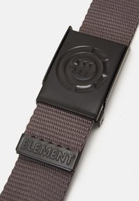 Cinturón de tela tejida gris con una hebilla de metal negro que presenta un logo circular y un acento de goma negra etiquetado "ELEMENT."