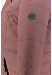 Chaqueta acolchada rosa con textura de acolchado horizontal, detalle de cremallera negra y un parche de logo redondo en la parte superior del brazo. Acabado de tela suave.