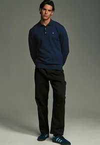 Tummansininen pitkähihaisen polo paidan kolmonnapainikkeinen kaulus, yhdistetty mustiin housuihin ja teal-värisiin Adidas-tennareihin. Yksinkertainen muotoilu, yhtenäiset värit ja pehmeä rakenne.