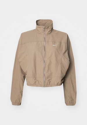 Cropped, beige Nike jacket with a high collar, full front zipper, elastic cuffs, and a small logo on the left chest. Textured fabric.