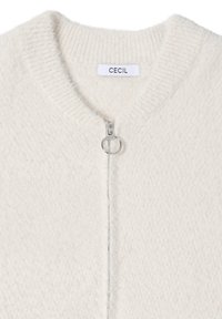 Jasnobeżowy kardigan na zamek wykonany z miękkiej, teksturowanej tkaniny. Posiada prążkowany dekolt oraz okrągły srebrny suwak. Metka z napisem "CECIL".