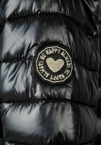 Juoda pūkinė striukė su blizgiai siūtu audiniu. Įtraukta apvalia siuvinėta etikete su širdies emblema ir tekstu "Būk laimingas."