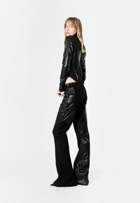 Top largo de manga larga de cuero sintético negro con cuello alto y detalle de corte. Combinado con pantalones negros con acentos de cuero y piernas acampanadas.