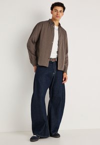 Camisa de botón rayada con cuello, llevada sobre una camiseta blanca, combinada con jeans de mezclilla oscuros de pierna ancha y zapatillas navy.