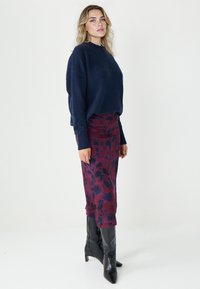Marineblauer Strickpullover kombiniert mit einem bordeauxroten, mit Blumen bedruckten Rock und kniehohen schwarzen Stiefeln mit Absatz. Schlichte, maßgeschneiderte Silhouette mit strukturiertem Stoff.