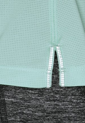 Light green textured fabric with small reflective strips bordering a small side slit over dark gray knit fabric.