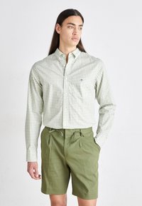 Cămașă verde în carouri cu butoni, având un buzunar pe piept, asortată cu pantaloni scurți verzi măslinii, cu talie elastică și croi lejer.