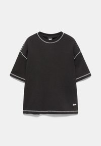 T-shirt noir à manches courtes avec surpiqûres blanches contrastantes et un petit logo blanc près de l'ourlet inférieur sur un fond uni.