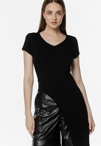 Czarna bluzka z dekoltem w serek i krótkim rękawem, z asymetrycznym wykończeniem u dołu oraz miękką teksturą, zestawiona z błyszczącymi czarnymi szortami z materiału skóropodobnego.