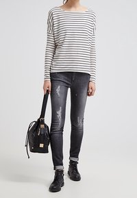 Gestreepte lange mouwen top, lichtgewicht stof; zwarte en grijze versleten skinny jeans; zwarte bucket bag; zwarte veterlaarzen tot de enkel.