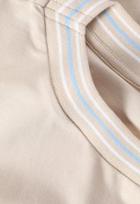 Beige stof med en glat tekstur, der har en krave med blå og hvide striber. Sømmen er synlig, hvilket fremhæver beklædningens design.