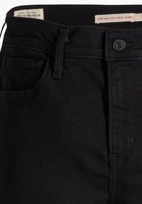 Jean super skinny noir taille haute avec bouton devant, passants de ceinture et étiquettes de marque visibles à l’intérieur de la ceinture.