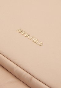 Tissu texturé rose pâle avec des lettres dorées embossées à la surface formant "ANNA FIELD".