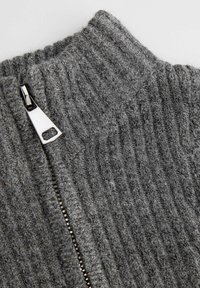 Szary sweter rozpinany na zamek z dzianiny o prążkowanej fakturze. Posiada srebrny zamek z trójkątnym uchwytem i wysoki kołnierz.