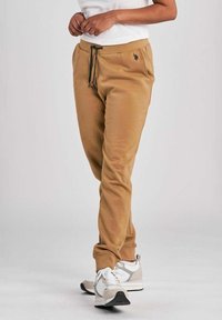 Jogger in cotone di un beige caldo con vita elasticizzata, cordino e tasche laterali. Abbinati a sneakers grigie e bianche.