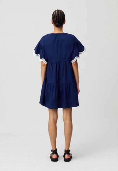 Vestido de algodón azul marino con mangas con volantes, cintura fruncida y borde de encaje blanco a lo largo de los extremos de las mangas. Textura suave, diseño hasta la rodilla.