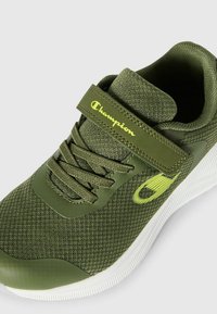 Scarpa sportiva verde con tomaia in rete e suola in gomma. Presenta un cinturino in velcro, design con lacci e logo Champion di colore verde chiaro.
