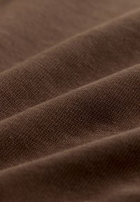 Nahaufnahme eines braunen Strickstoffs mit detaillierter Textur und feiner Naht sowie weichen Falten.