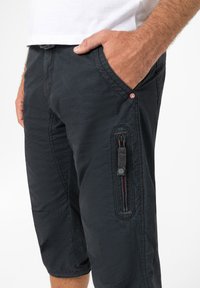 Dunkle, leichte Shorts mit einer strukturierten Oberfläche, einschließlich Seitentaschen und einer Reißverschlusstasche. Mit einem kleinen Logo-Detail in der Nähe der Taille.