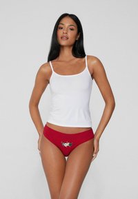 Braguitas de bikini rojas con bordados decorativos de temática festiva. La tela parece suave con una textura lisa, complementada por una camiseta sin mangas blanca.