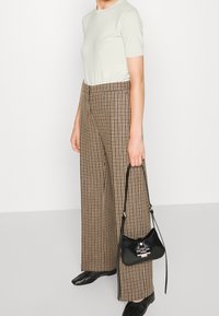 Chemise à manches courtes vert clair, pantalon large à carreaux marron, sac à main noir avec ferrures argentées, et chaussures noires à bout pointu.
