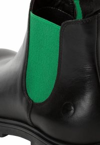 Bottine en cuir noir avec panneau latéral élastique vert, finition texturée, bout arrondi et semelle en caoutchouc avec légère sculpture.