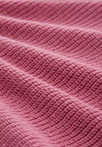 Coperta rosa a trama tessuta con motivo a coste diagonali, realizzata in materiale morbido, che mostra una profondità e una morbidezza variabili.