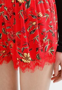 Pantaloni corti rossi con motivo floreale caratterizzati da un bordo in pizzo all'orlo, con una texture liscia e un tessuto leggero decorato con vari fiori e foglie colorati.