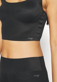 Sort sømløs sports crop top lavet af tekstureret materiale, med rund hals og et lille logo i nederste venstre hjørne.