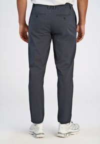 Pantalon bleu marine en tissu texturé, avec deux poches arrière dotées de fermetures à bouton et des jambes fuselées. Associé à des chaussures de sport blanches.
