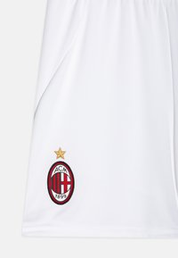 Weiße Sportshorts mit gesticktem AC Milan-Logo. Das Logo ist oval mit roten und schwarzen Streifen, einem goldenen Stern darüber und dem Jahr "1899."