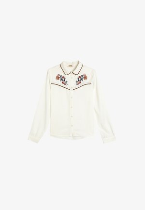 Witte button-up shirt met kleurrijke bloemenborduring op de borst en contrasterende bruine piping langs de kraag en schouders.