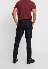 Ciemne spodnie w kratę o dopasowanym kroju, charakteryzujące się gładką fakturą i subtelnym wzorem w kratę. Uzupełnione dopasowanym t-shirtem w kolorze burgundowym i czarnymi butami.