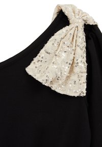 Crni top s teksturiranim čvorastim mašnom od bež tkanine, ukrašen svjetlucavim šljokicama. Naborani detalj na rukavima naglašava dizajn.