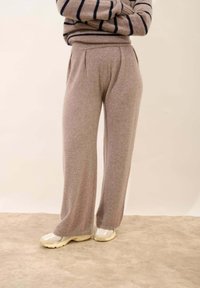 Šedé pletené kalhoty s širokými nohavicemi a měkkou texturou, mají vysoký pas a přední sklady, doplněné o světle barevné sportovní boty.