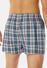 Boxer a quadri blu e bianchi con una cintura elastica, caratterizzati da un motivo a scacchi con accenti di rosso e blu scuro.