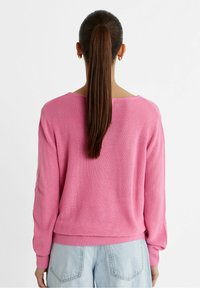 Pull en maille rose à manches longues avec texture côtelée, col rond et ourlet élastique, porté avec un jean bleu clair.