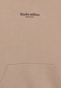 Felpa in cotone beige con tasca frontale, con la scritta "Studio edition" e le coordinate "55°57'03"N" stampate in nero.
