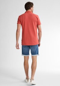 Koraalkleurige polo met korte mouwen, denim shorts met omgeslagen zoom, en witte sneakers met tan accenten. Schoon ontwerp, casual pasvorm.