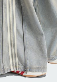 Light blue denim pants with white side stripes and a zipper at the hem partially covering white sneakers with red stripes.